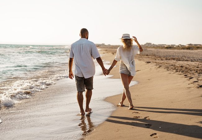 Young beautiful couple walking on beach near sea at sunset