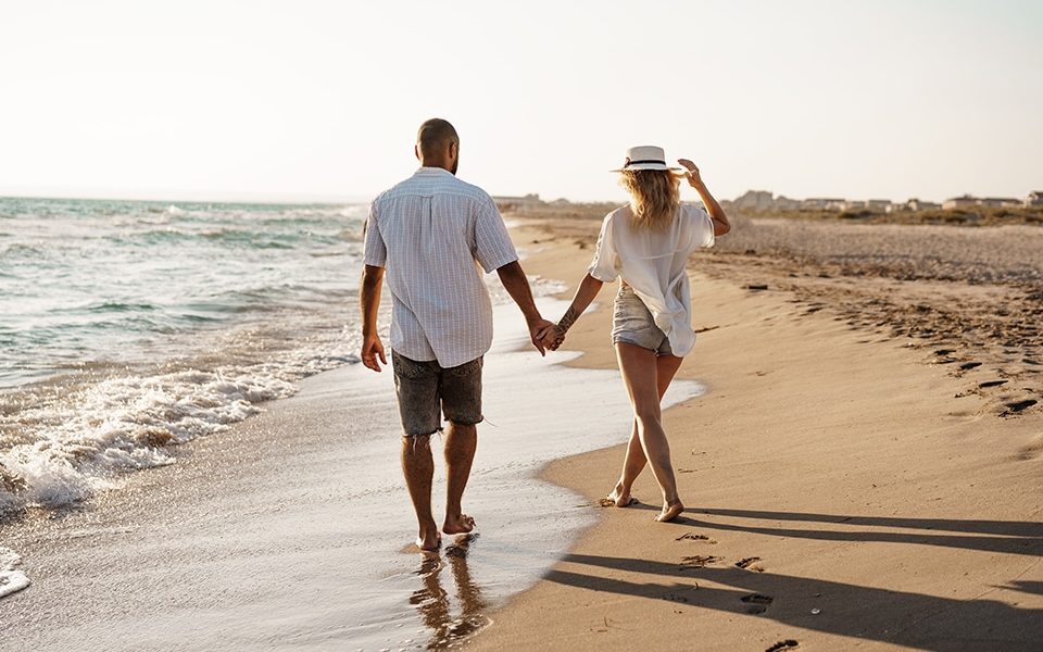 Young beautiful couple walking on beach near sea at sunset